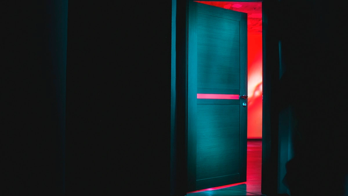 A dark door stands open onto a glowing red-lit room beyond. — a The Obsidian Key guide to The Assumed State: Identity Instead of Requesting.