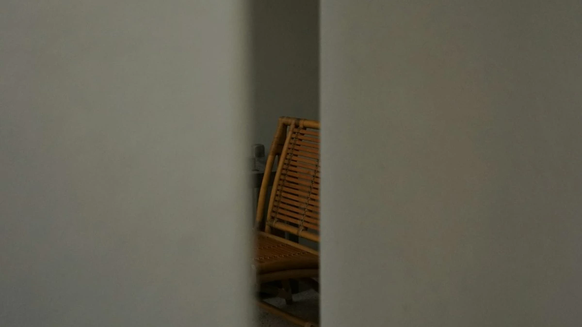 A wooden chair glimpsed through a narrow opening between pale walls. — a The Obsidian Key guide to Assumption 101: I Am the Man Who.