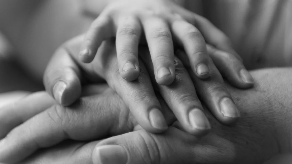 Three hands of different generations resting stacked together in soft black-and-white light. — a The Obsidian Key guide to The Body’s Role in Manifestation.