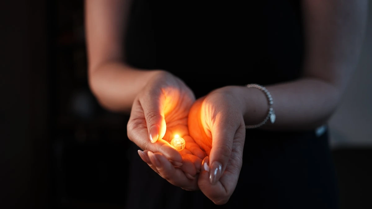 Two cupped hands holding a small glowing flame in a dark room. — a The Obsidian Key guide to The Drowning Man and Money: Wanting Like Air.