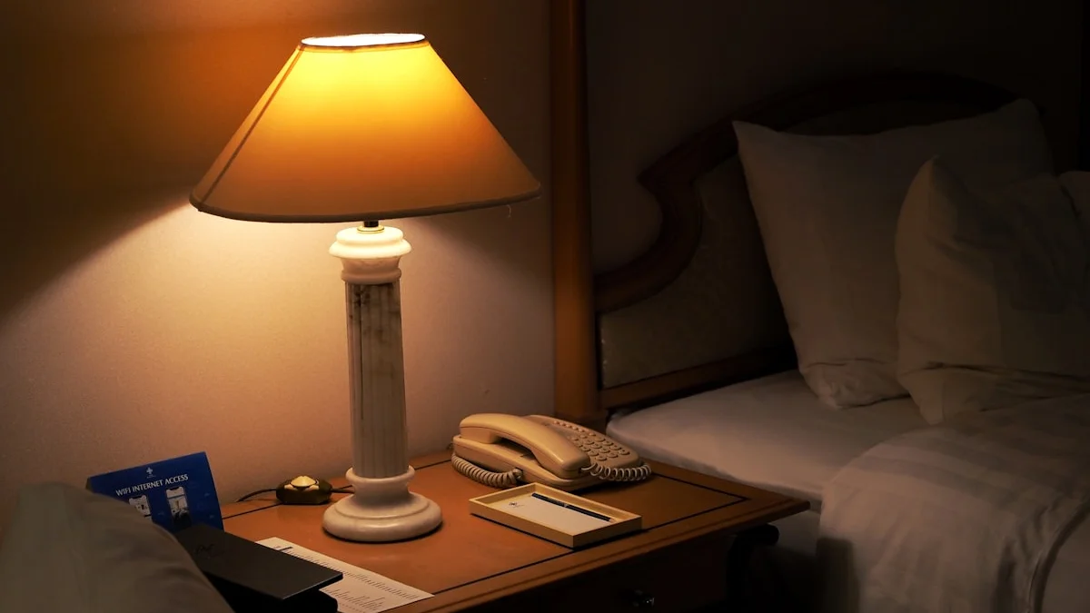 A warm amber lamp glows on a bedside table next to a bed at night. — a The Obsidian Key guide to The Evening Replay: Re-Authoring the Day Before Sleep.