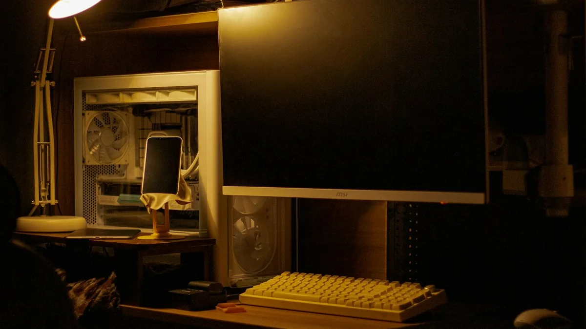 A dark desk at night with a switched-off monitor, keyboard, and a phone on a stand under a small warm lamp. — a The Obsidian Key guide to The Feed: Attention Delivered at a Stranger's Ranking.