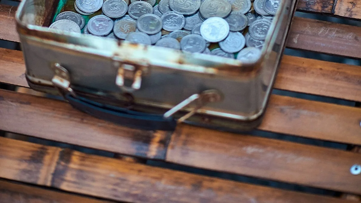 An open vintage tin box filled with old coins resting on a wooden bench. — a The Obsidian Key guide to The First Thousand: Seed of a Wealth Posture.