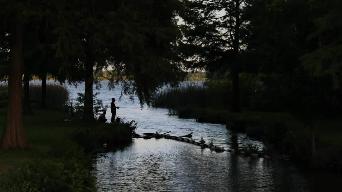 A lone figure stands silhouetted beside a calm river inlet at dusk. — a The Obsidian Key guide to How to Run the Opened Hand Working Day by Day.