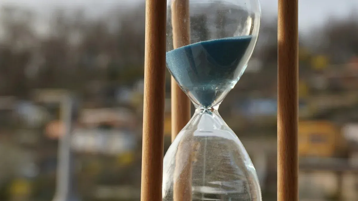 A wooden-framed hourglass with blue sand against a soft blurred background. — a The Obsidian Key guide to Why the Morning Seat Is Worth Three Evening Seats.