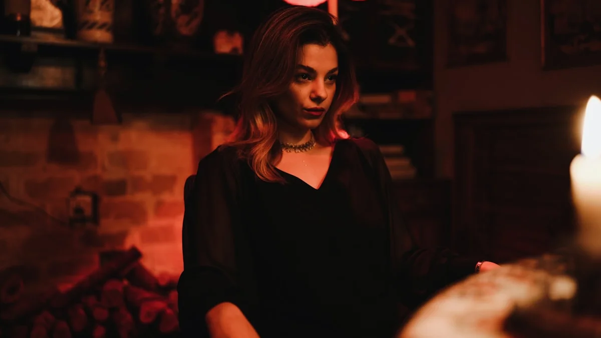A woman in a black blouse sits beside a lit candle in a dim, warm room. — a The Obsidian Key guide to Working the Ninth Law With People: A Companion.