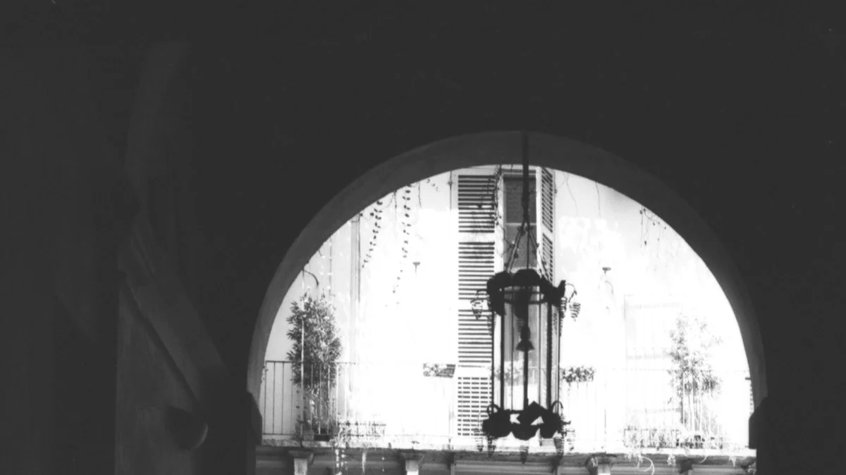An iron lantern hangs in a stone archway opening onto an old sunlit courtyard. — a The Obsidian Key guide to The Glossary of the Doctrine in The Obsidian Key.