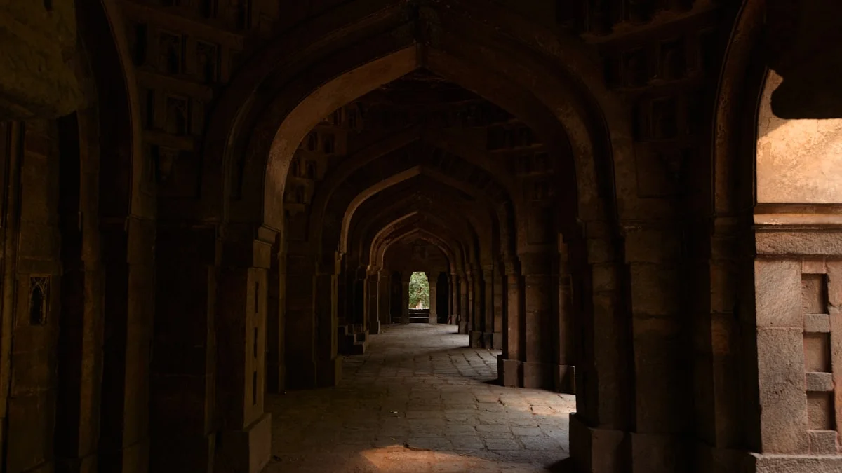 A long dark stone corridor of repeated arches recedes into shadow in an ancient building. — a The Obsidian Key guide to What the Order Knew About Nights and Their Sealing.