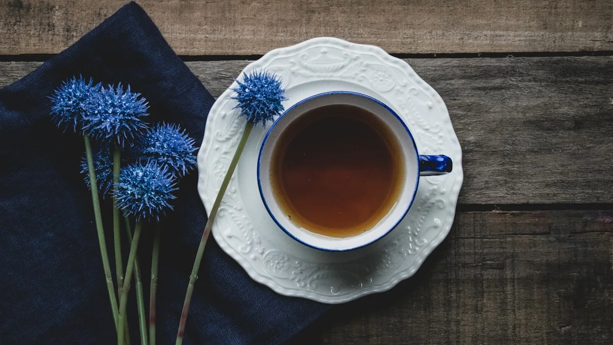 A blue-rimmed teacup on a white china saucer beside blue thistle flowers on a dark wooden table. — a The Obsidian Key guide to Partners and the Assumed State: A Field Guide.