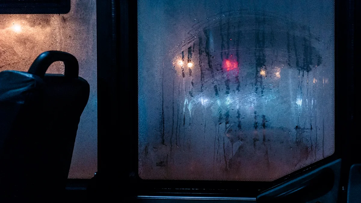 A fogged window pane streaked with condensation at night, blurred street lights and one red signal glowing beyond the glass. — a The Obsidian Key guide to Signs Others Notice Before You Say a Word.