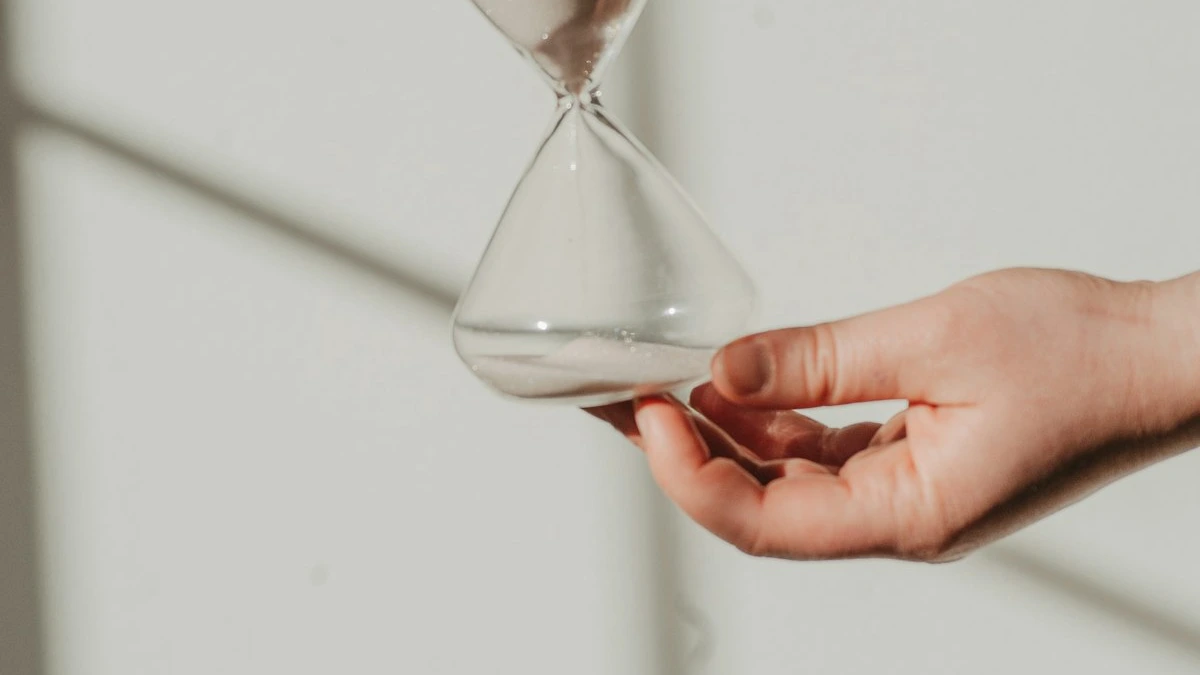 A hand holding a glass hourglass in soft window light. — a The Obsidian Key guide to The Compound Rite: Twenty-One Days Defined.