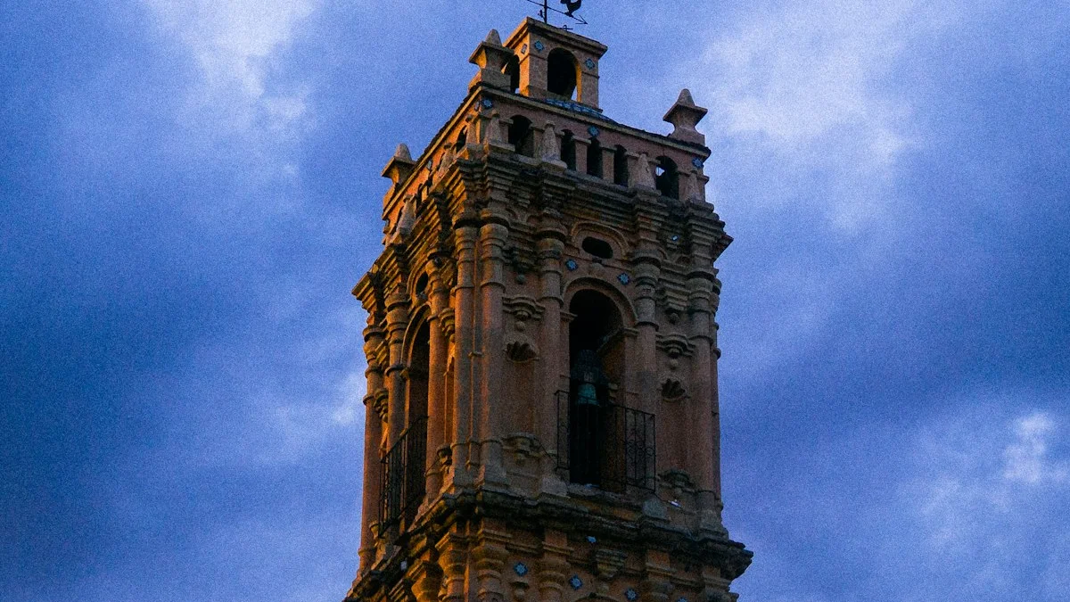 An ornate old bell tower lit by the last warm light against a deep blue dusk sky. — a The Obsidian Key guide to The Halloway House: Night One in the Archive.