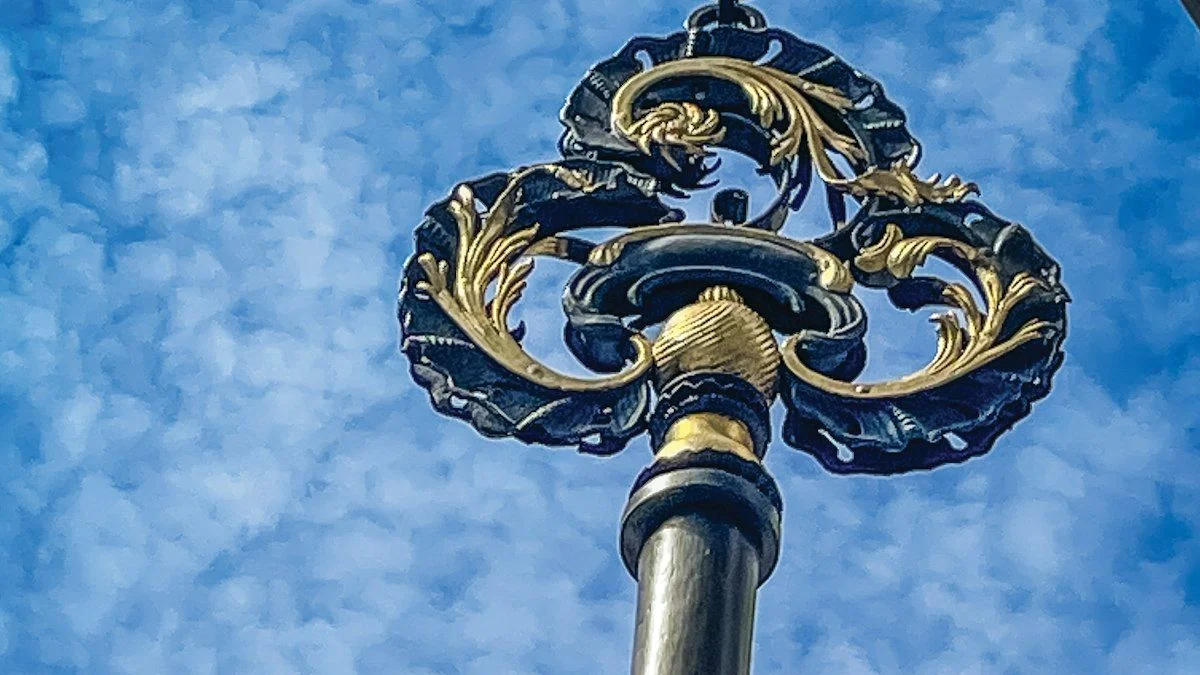 A large ornate wrought-iron key with gilded scrollwork against a blue cloudy sky. — a The Obsidian Key guide to The Key: The Daily Master Practice Defined.