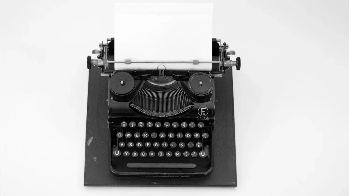 A black vintage typewriter with a blank white sheet of paper waits on a pale grey table. — a The Obsidian Key guide to The Nine Laws on One Line Each: A Pocket Reference.