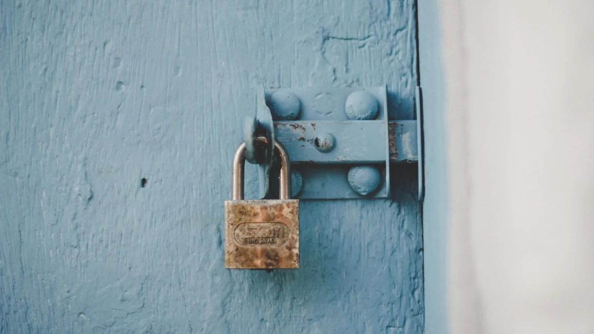 A rusted padlock snaps shut on the hasp of a pale blue wooden door. — a The Obsidian Key guide to The Sealing: Seven Days on Three Holes.