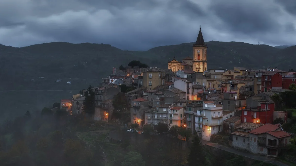 A hilltop village glows with lamplight under a dark evening sky. — a The Obsidian Key guide to The Shield Operation Companion: Beyond the Introductory Form.