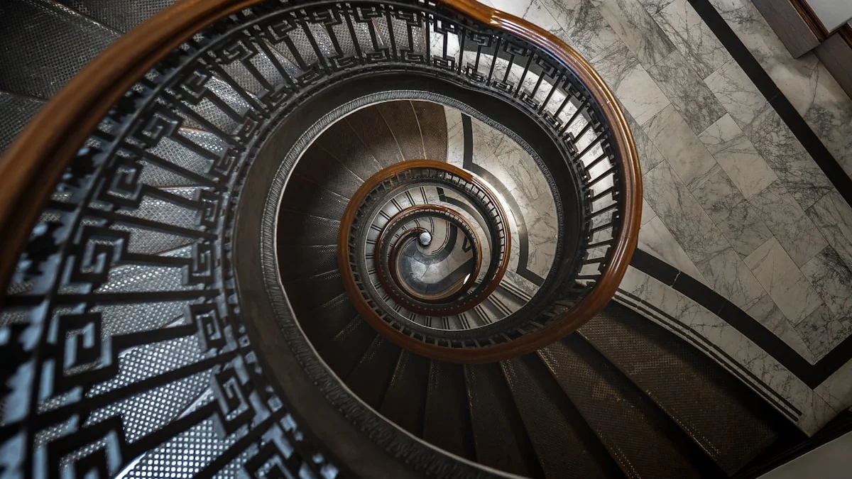 An ornate spiral staircase with a wooden handrail winding down to a marble floor. — a The Obsidian Key guide to Second Cycles: Re-Running the Path With the Book.