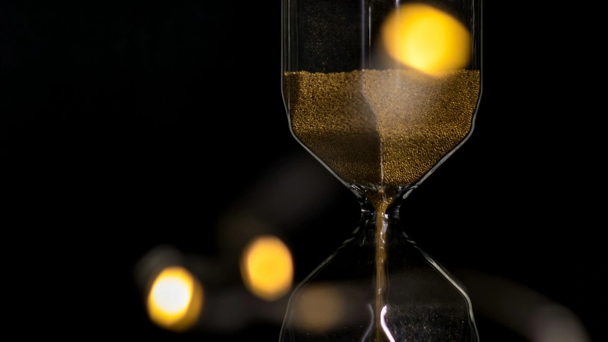Gold sand falls through a glass hourglass against a black background with warm amber lights glowing behind. — a The Obsidian Key guide to Urgency Is a Borrowed Clock: Reclaim Your Own Pace.