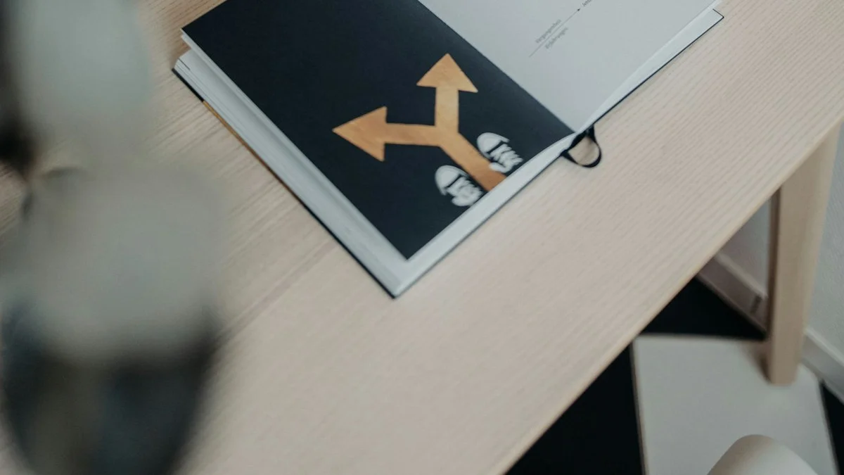 An open book printed with a golden two-arrow signpost lies on a pale wooden desk beside a potted plant. — a The Obsidian Key guide to What Is Manifestation According to the Doctrine.